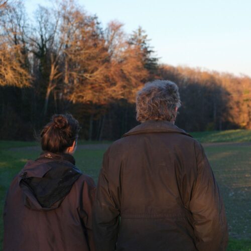 Ausserfamiliäre Hofübergabe, eine alte und eine junge Person schauen auf ein Feld, Sonnenuntergang
